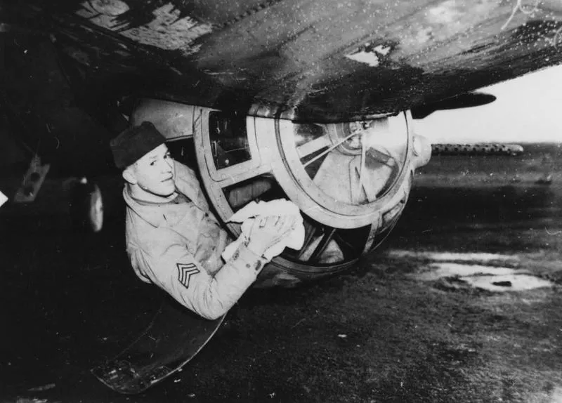 Staff Sergeant Max Armstrong, an assistant crew chief of the 91st Bomb Group, cleans the ball turret of a B-17 Flying Fortress. Image stamped on reverse: 'Passed for publication 1 Feb 1943.' Printed caption on reverse: 'Some of the airmen from American who are taking part in the daily raids on enemy occupied territory and Germany, in their giant high altitude aircraft the "Flying Fortress" capable of carrying a 11,000 [a censor has corrected this figure beneath to say '10,000] pound bomb load. Photo shows